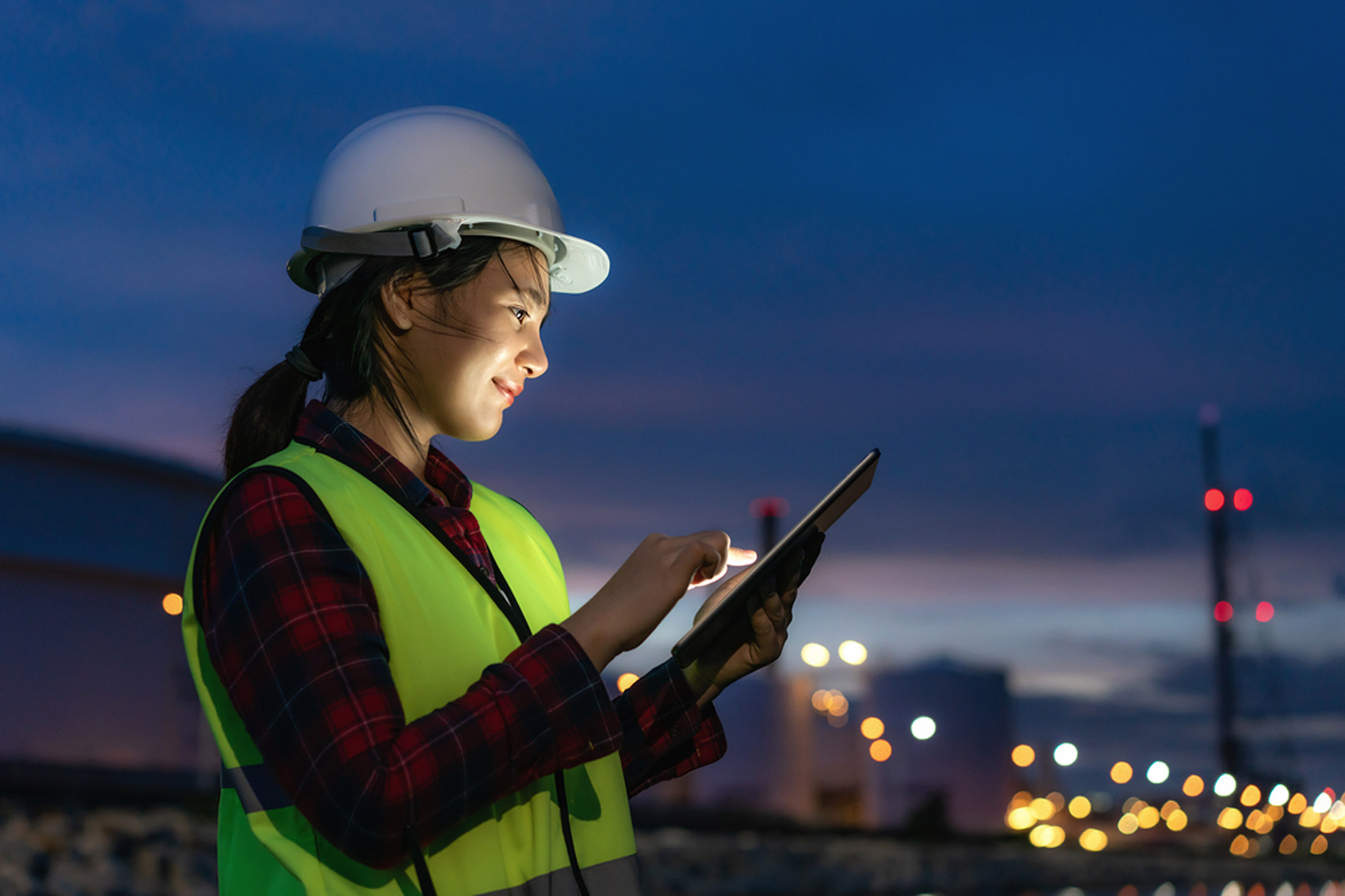 Asian woman petrochemical engineer working at night with digital tablet Inside oil and gas refinery plant industry factory at night for inspector safety quality control.